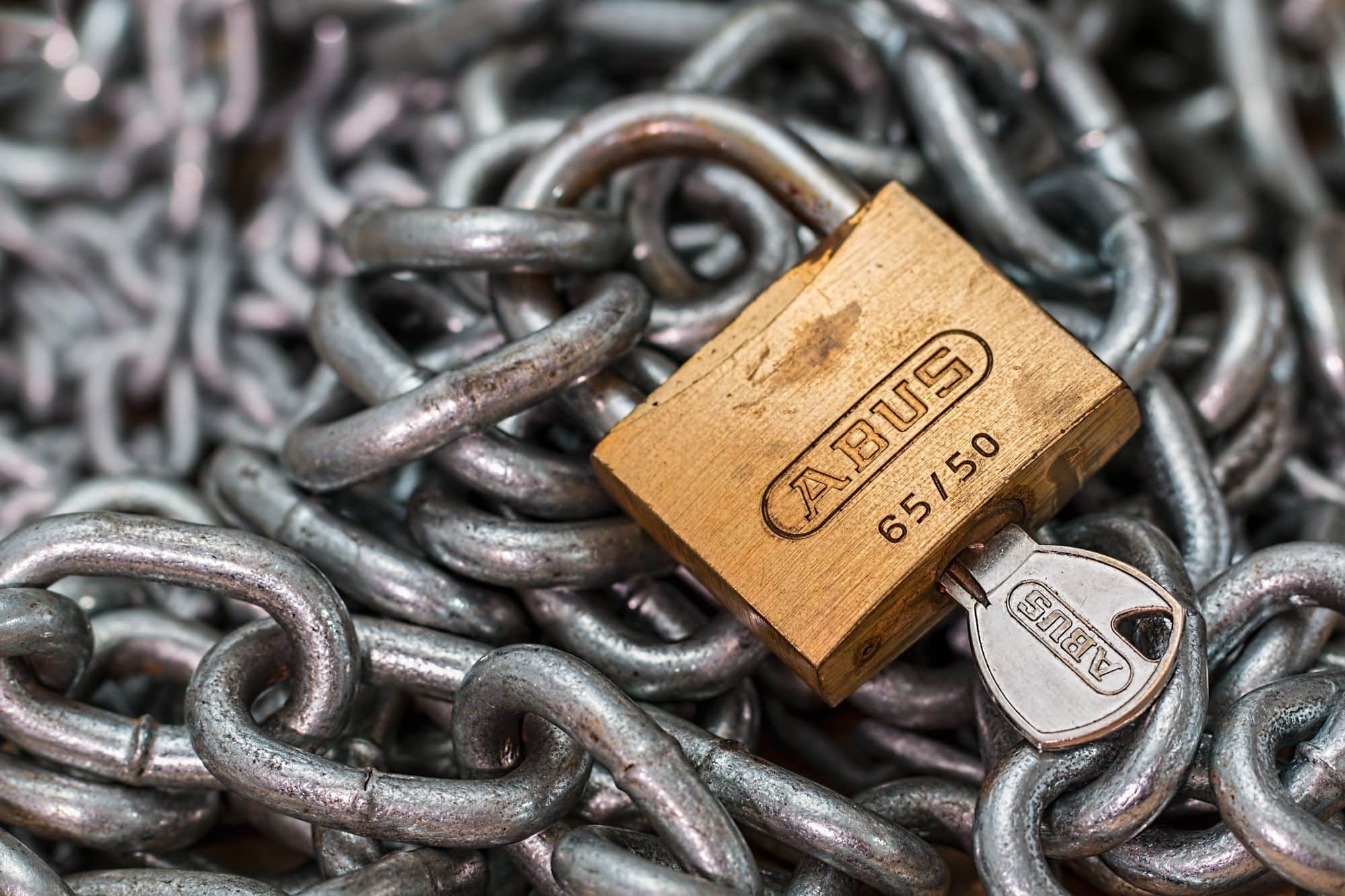 A brass padlock and key hold a heavy metal chain.