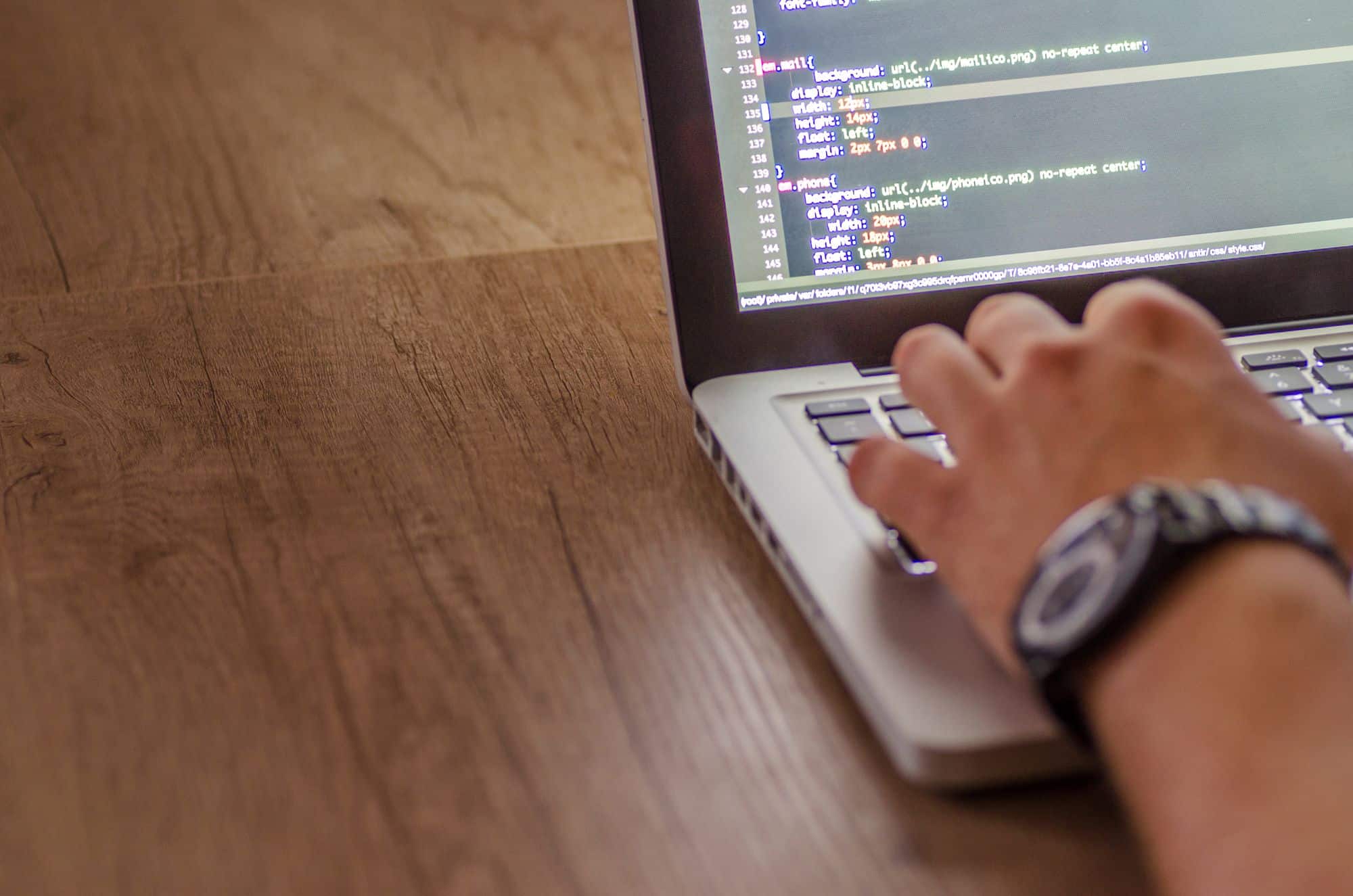 Hands on a laptop keyboard with programming code on the screen.