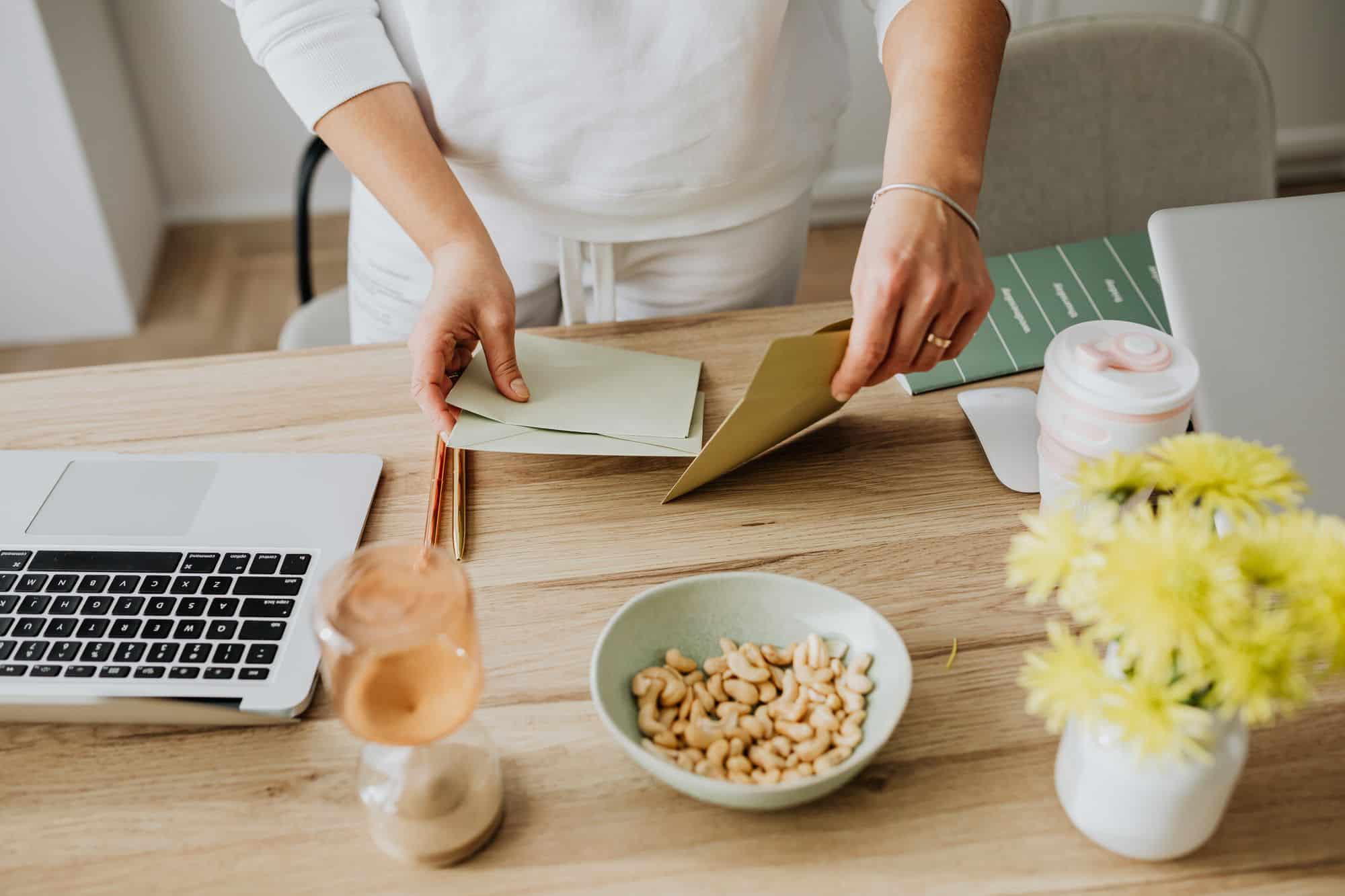 A person handles envelopes at a desk beside a laptop.