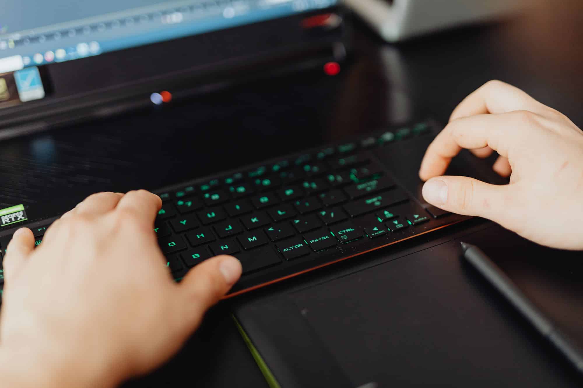 Hands typing on an illuminated computer keyboard.