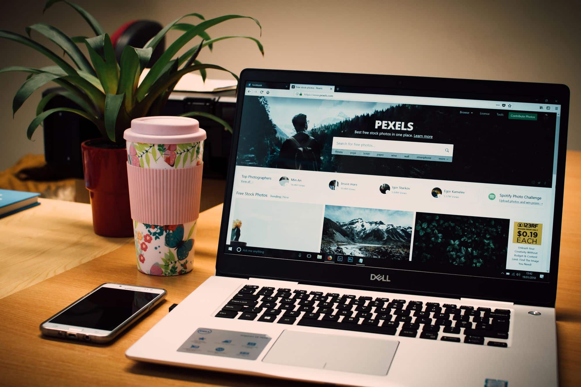 A laptop displaying Pexels beside a smartphone on a wooden desk.